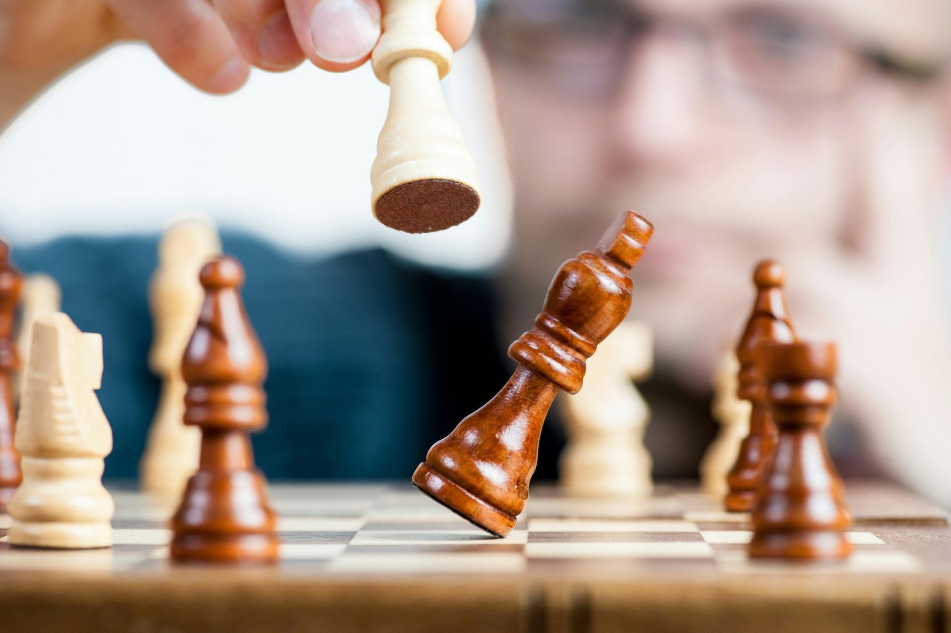 Chess player knocking over black king with a white king piece on a chessboard.