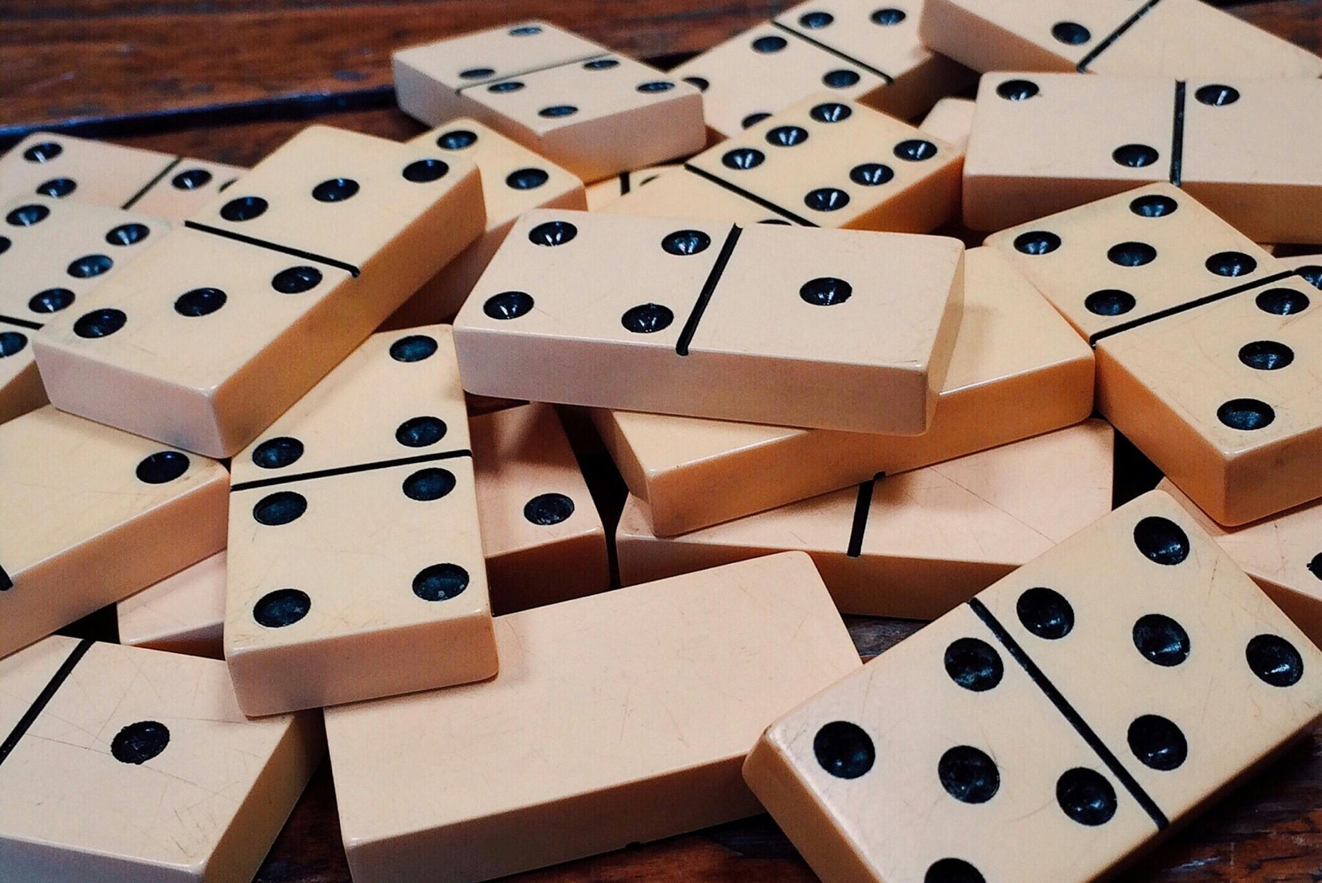 Pile of light-colored dominoes with black dots, scattered on a wooden surface.