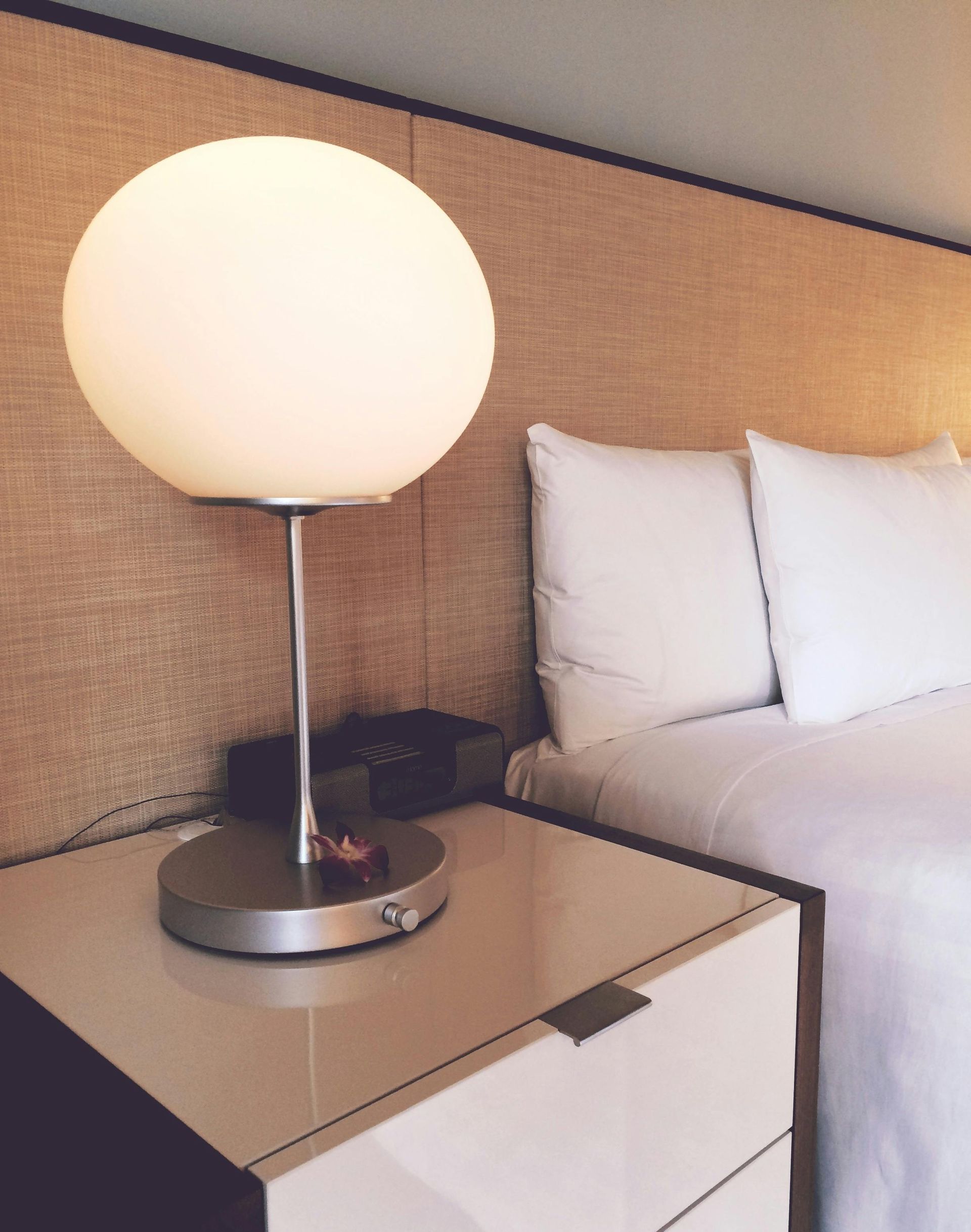 A glowing orb lamp sits on a bedside table next to a bed with white linens and pillows.