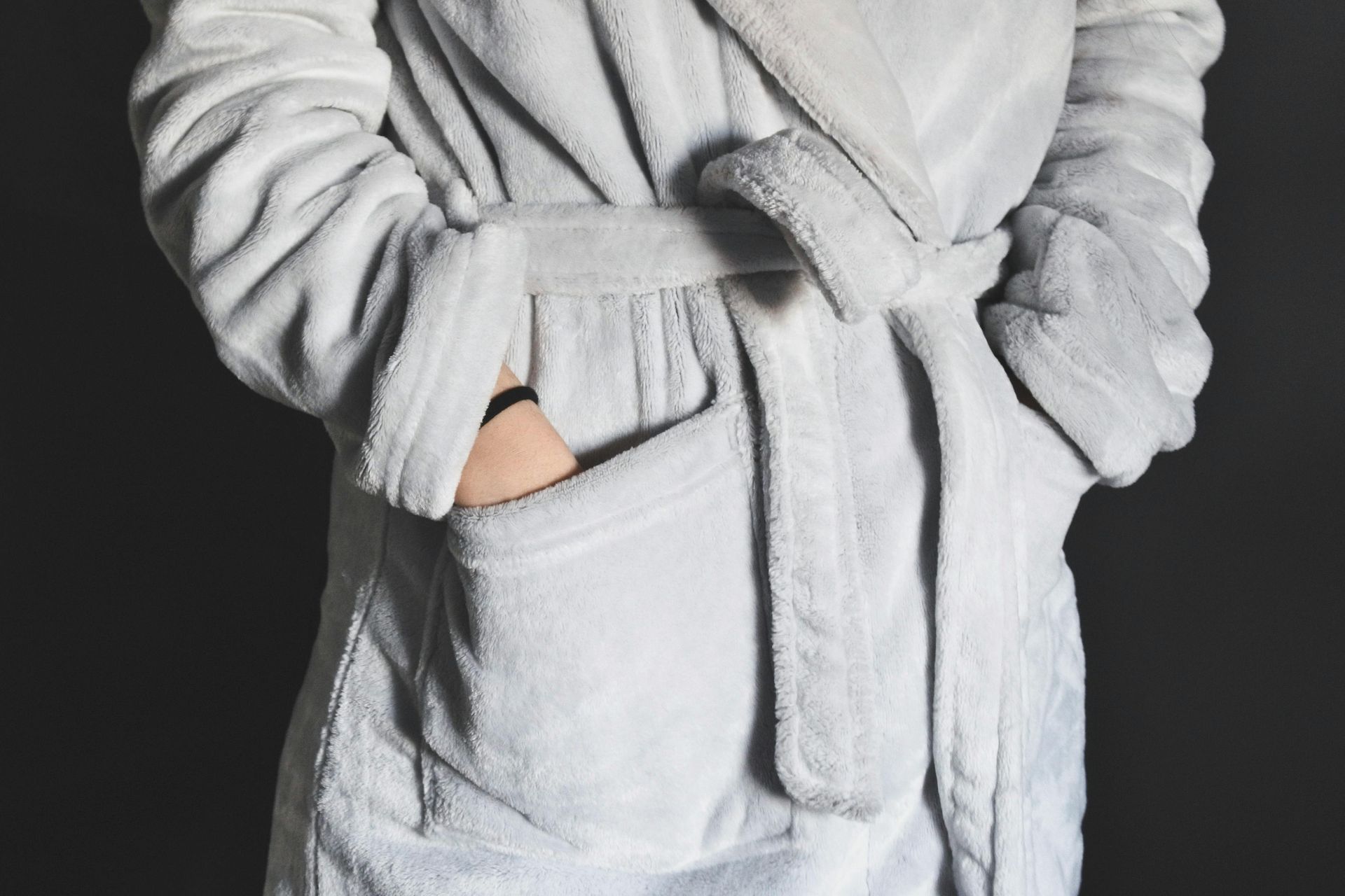 Person in light gray robe with hand in pocket, black background.