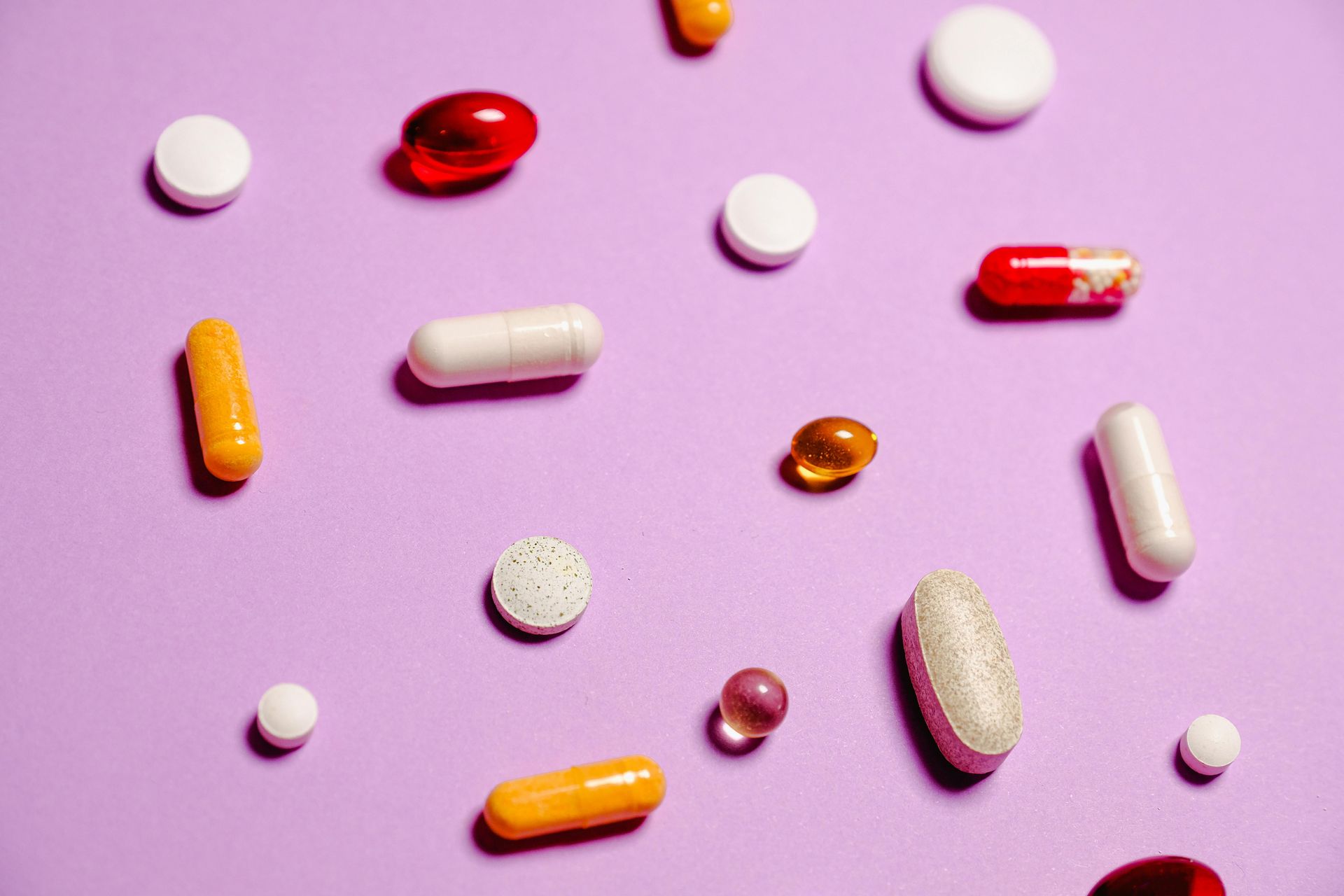 Various pills and capsules scattered on a purple surface.