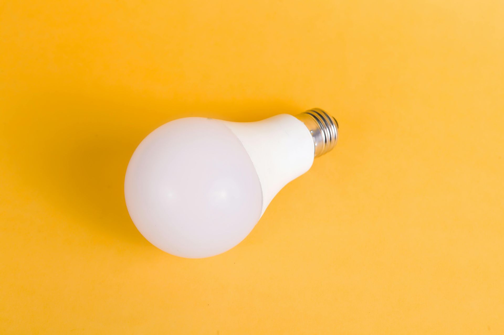 White LED lightbulb with a silver base, laying on a solid yellow background.