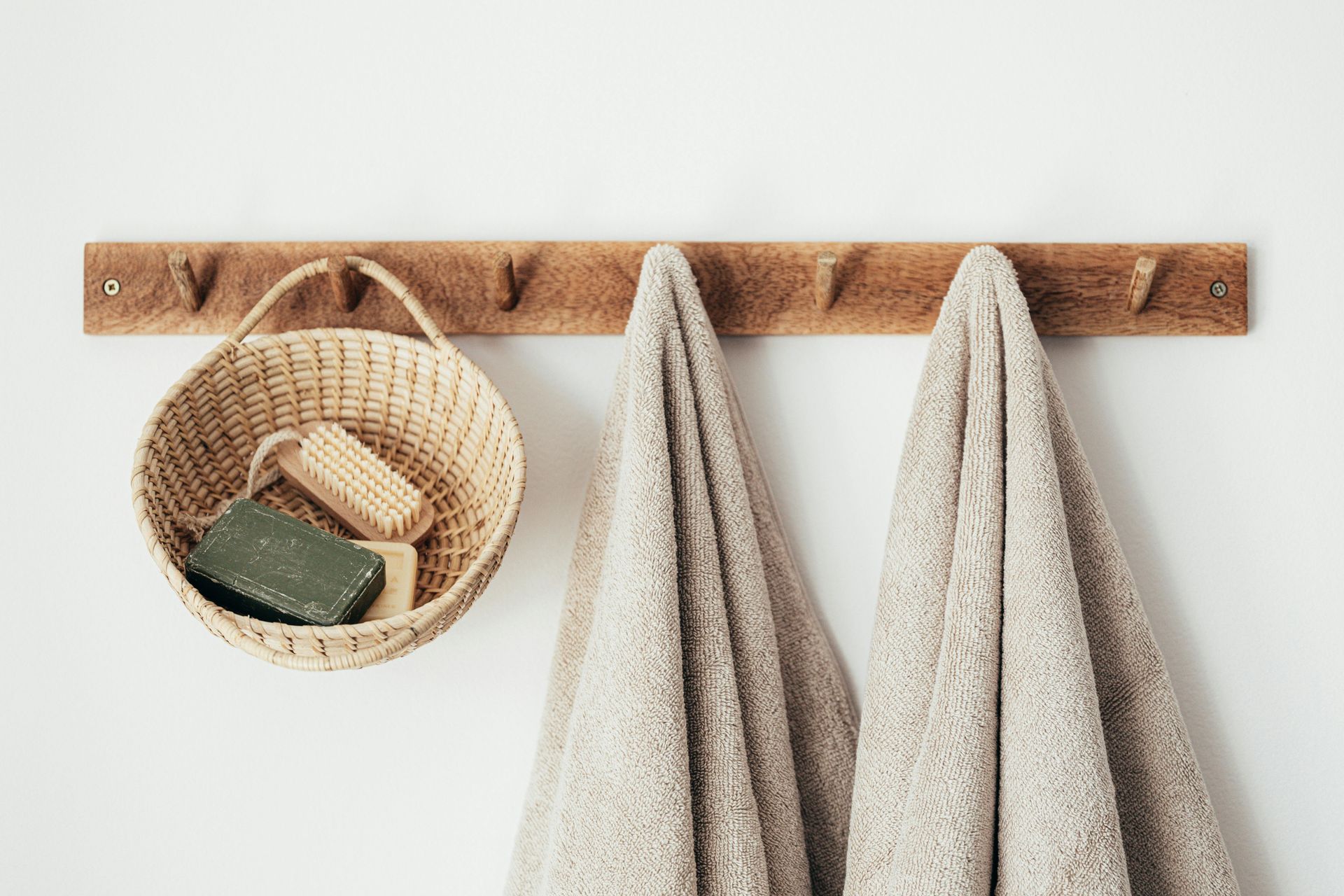 Wooden rack with towels and a basket containing soap, hanging against a white wall.