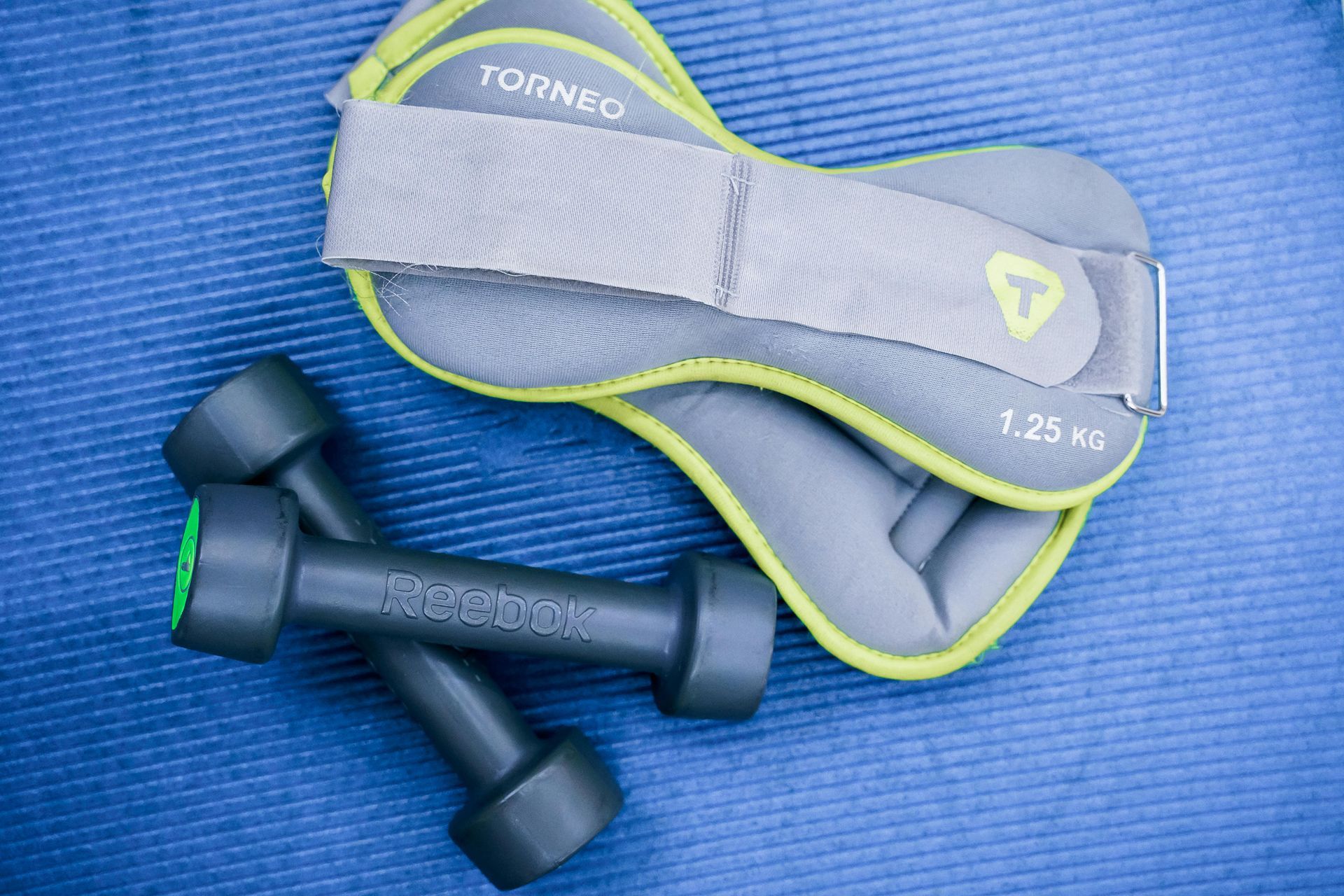 Two small gray dumbbells and a gray ankle weight on a blue mat.