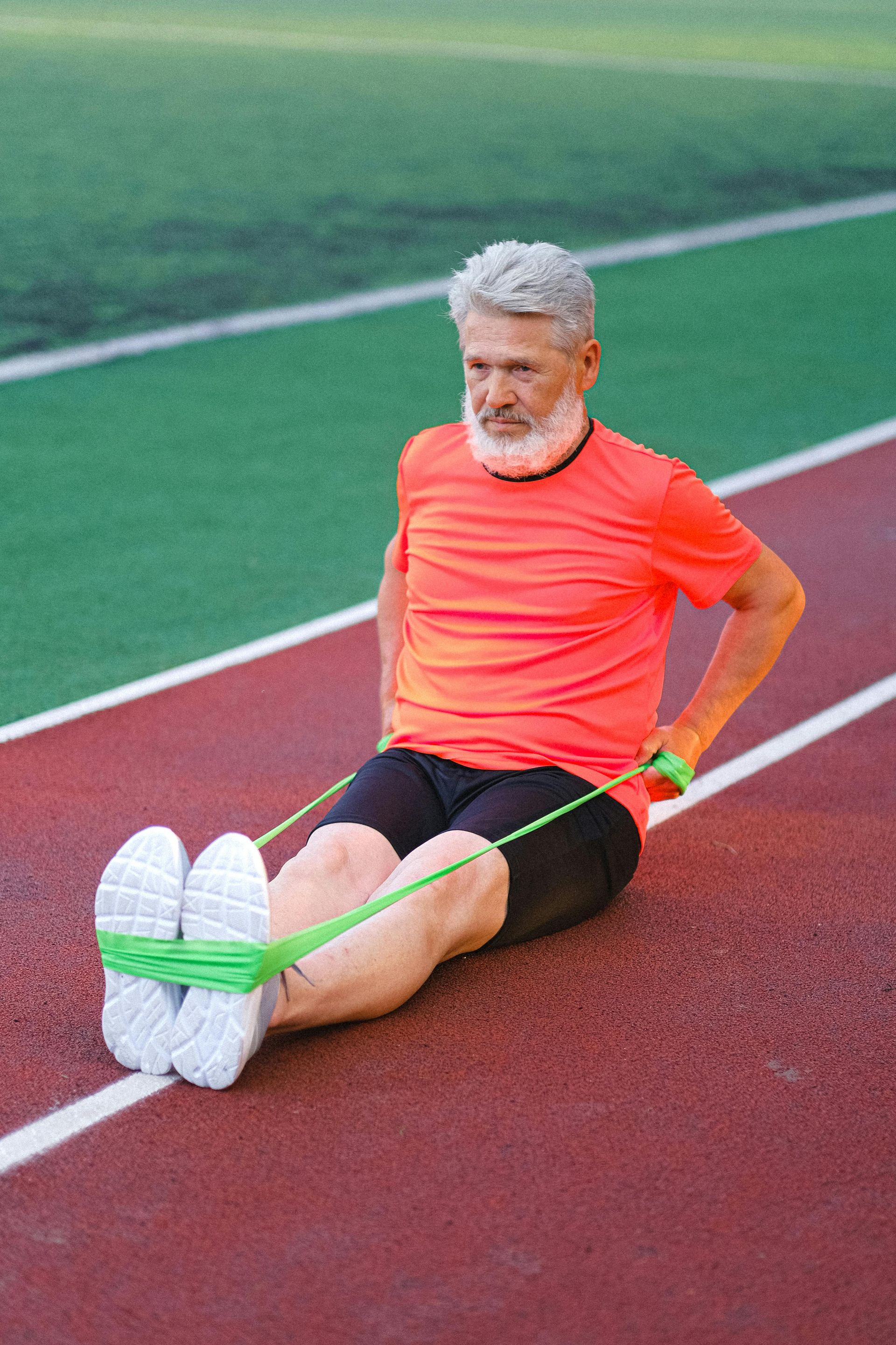 Man with gray hair and beard exercising with resistance band on a track.