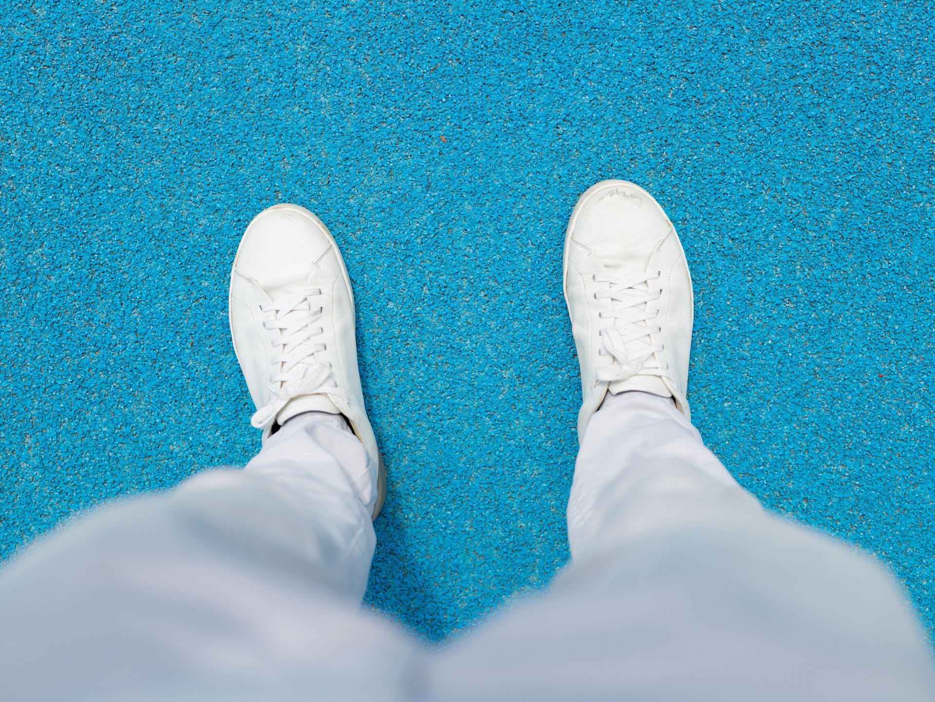 White sneakers and pants on a blue, textured surface, viewed from above.