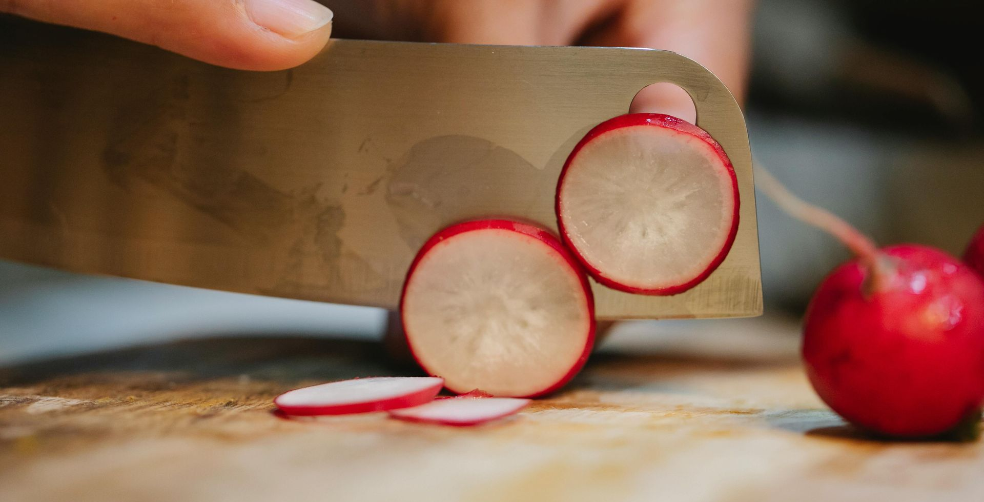Chopping radishes on a wooden cutting board with a large knife.
