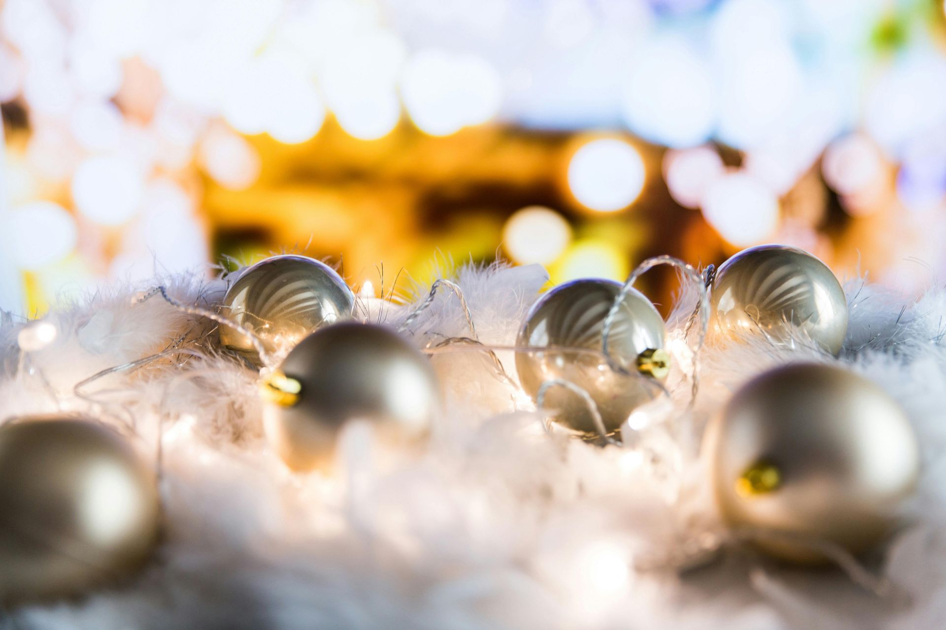 Gold Christmas ornaments on white fluff, with string lights and blurred background.