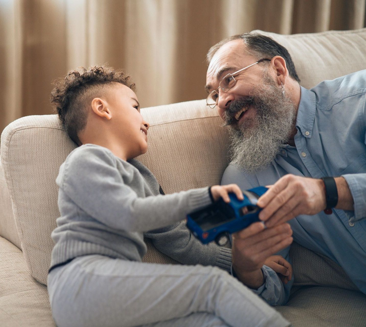 A young boy and an older man sharing a blue toy car.