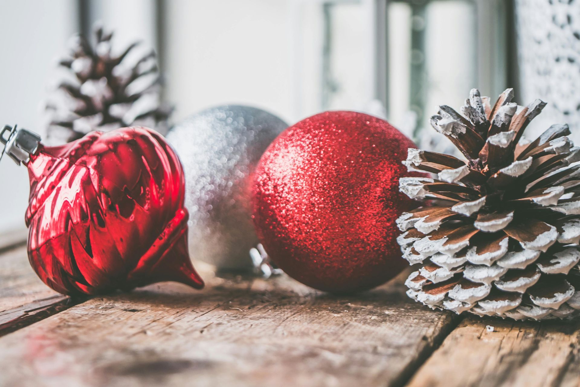 Red and silver Christmas ornaments and pinecones on a rustic wooden surface.