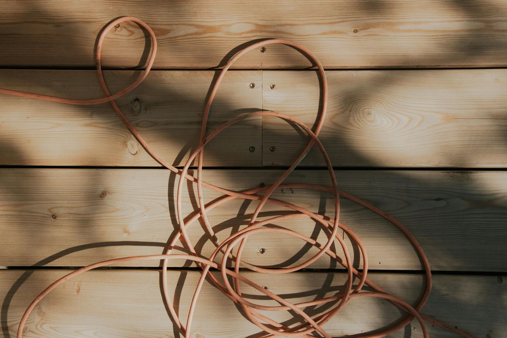 Coiled orange electrical cord on light-colored wooden planks with shadows cast across.