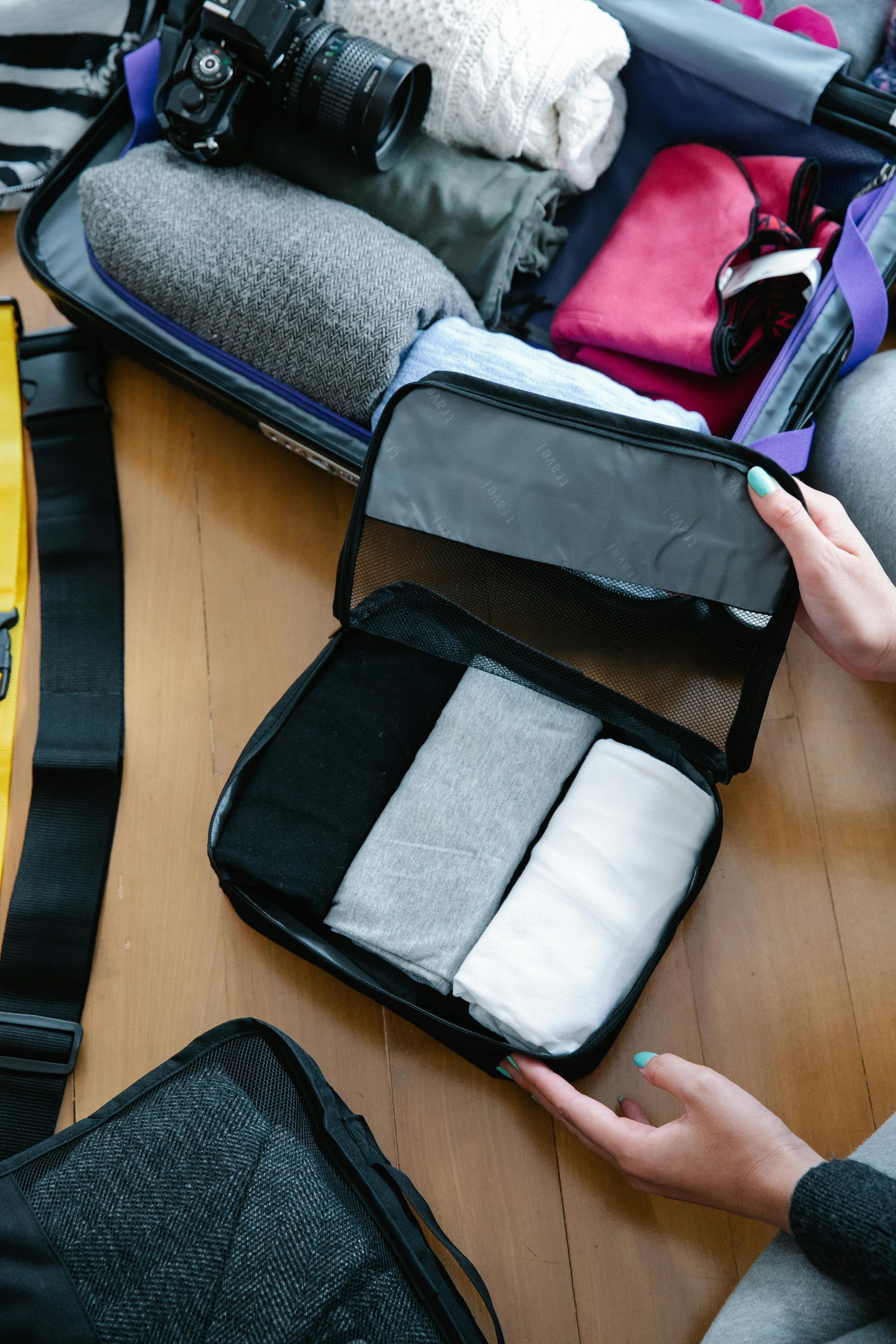 Person packing luggage; hands holding open travel cube with rolled socks.