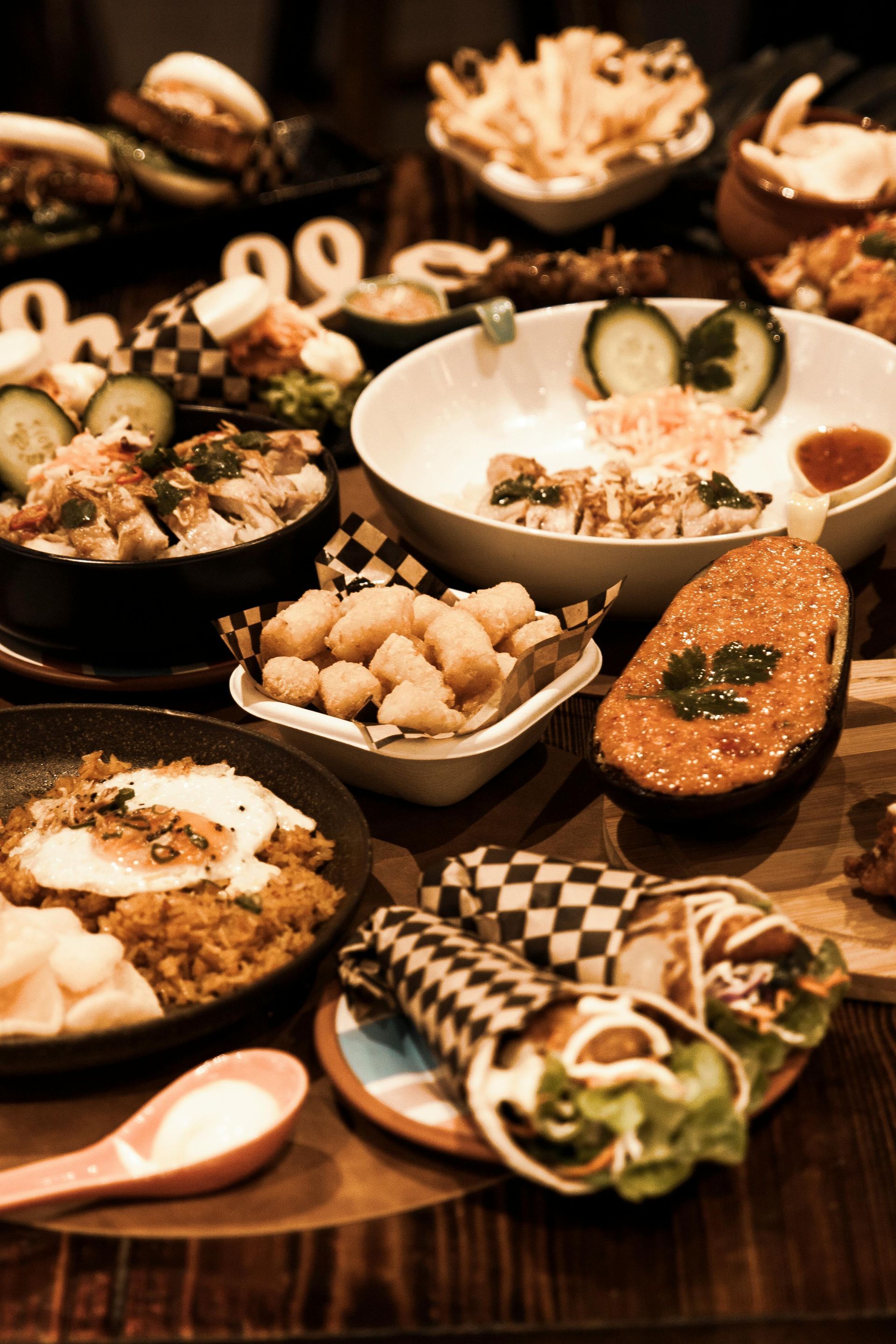 Table of assorted food: bowls, fries, wraps, and an avocado on a wooden surface.