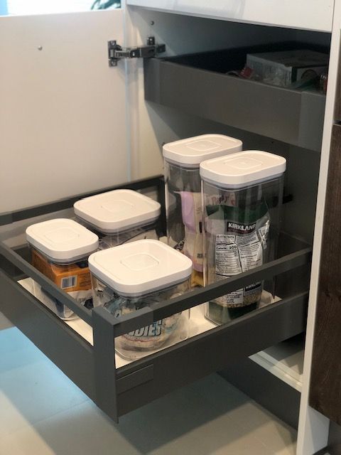 Gray pull-out kitchen drawer with clear containers, mostly white lids, inside a white cabinet.