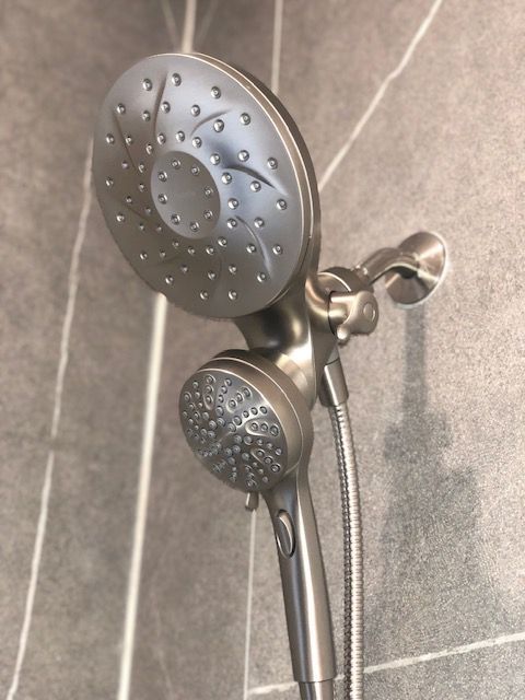 A dual showerhead in a brushed nickel finish against gray tiled wall.