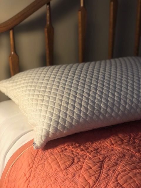 White quilted pillow on a bed with orange quilt and wooden headboard.