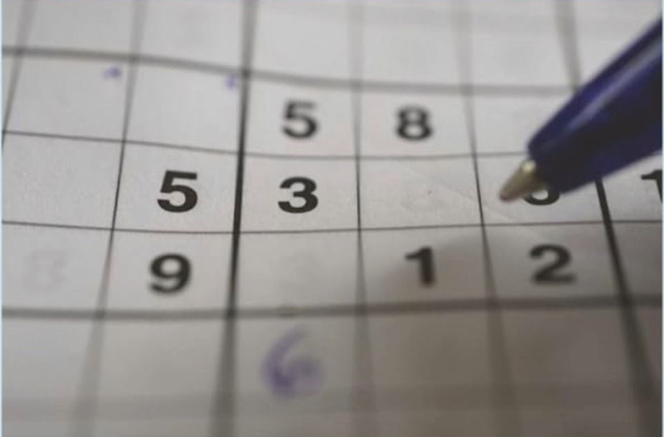 Sudoku puzzle with numbers and a pen filling in a cell.