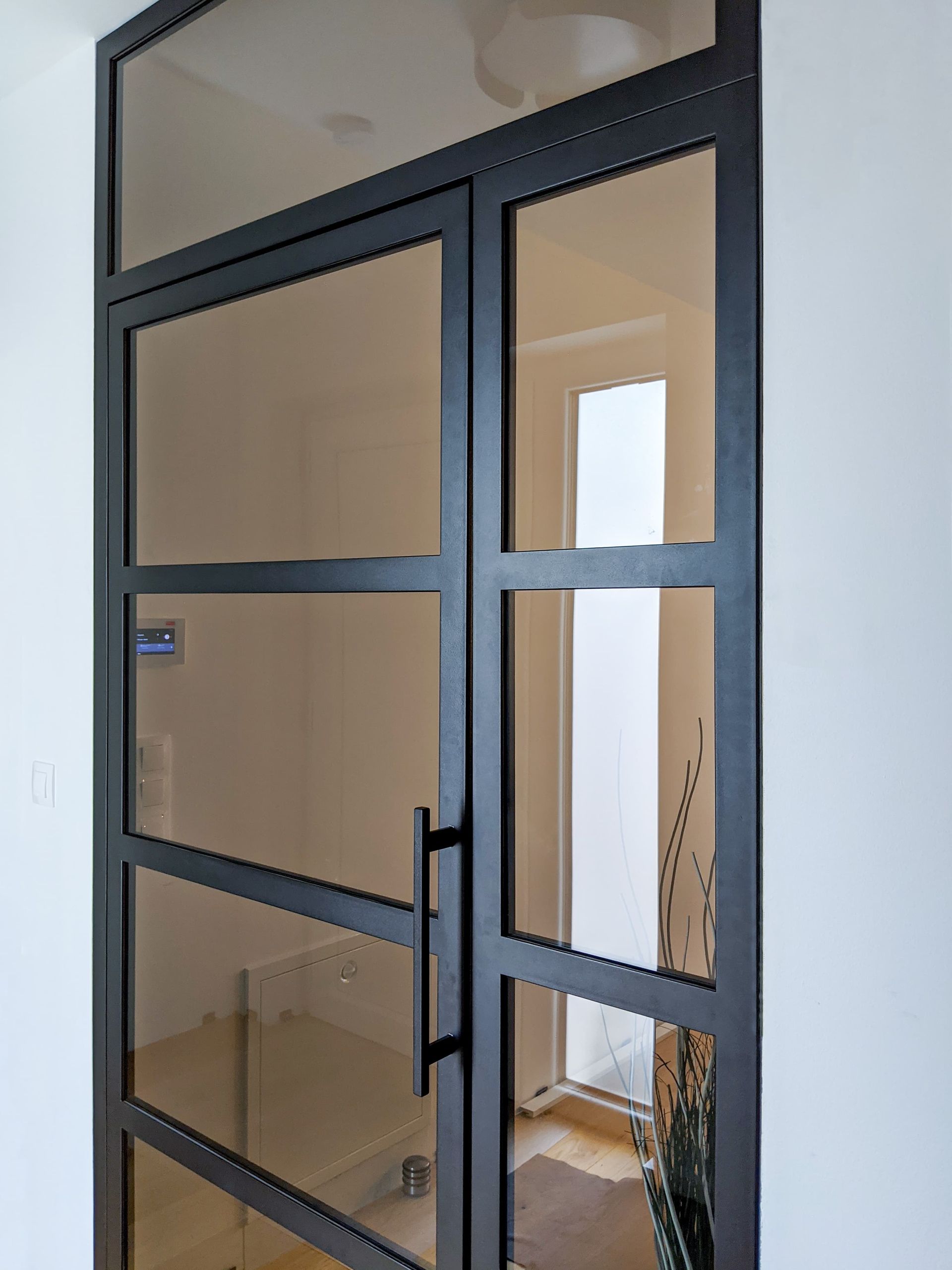Eingangstür aus schwarzem Glas mit Metallgriff im Flur