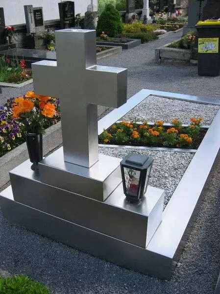 Moderner silberner Grabstein mit Laternen und orangefarbenen Blumen auf einem Friedhof
