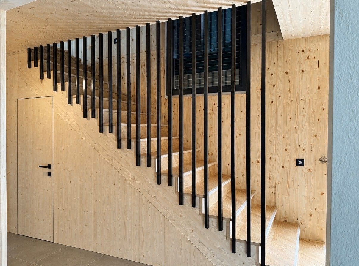 Moderne Treppe mit schwarzen, vertikalen Lamellen vor hellen Holzwänden, die eine geometrische Trennwand bilden.