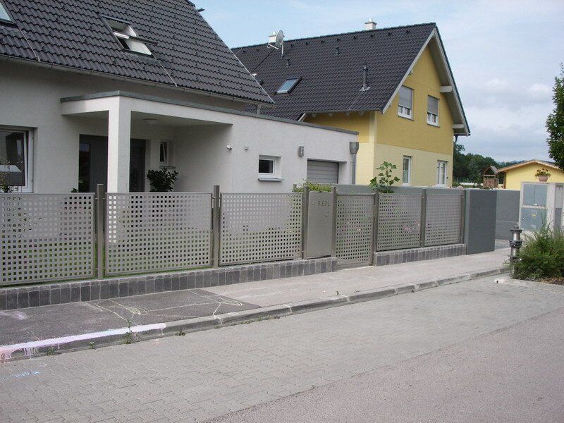 Wohnstraße mit modernen Häusern und einem grauen Metallzaun entlang des Gehwegs.