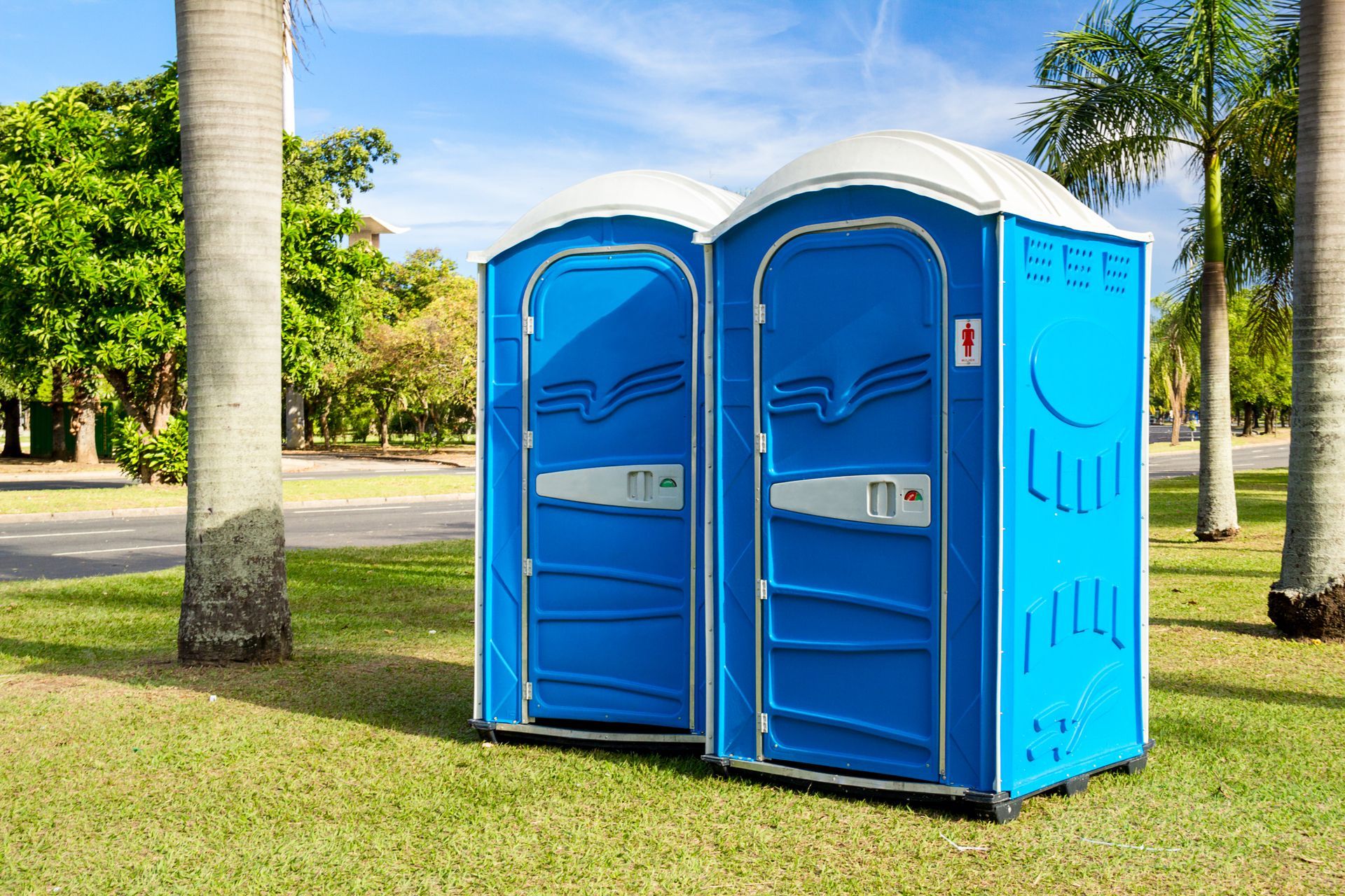 Two blue portable toilets are sitting next to each other in a park.