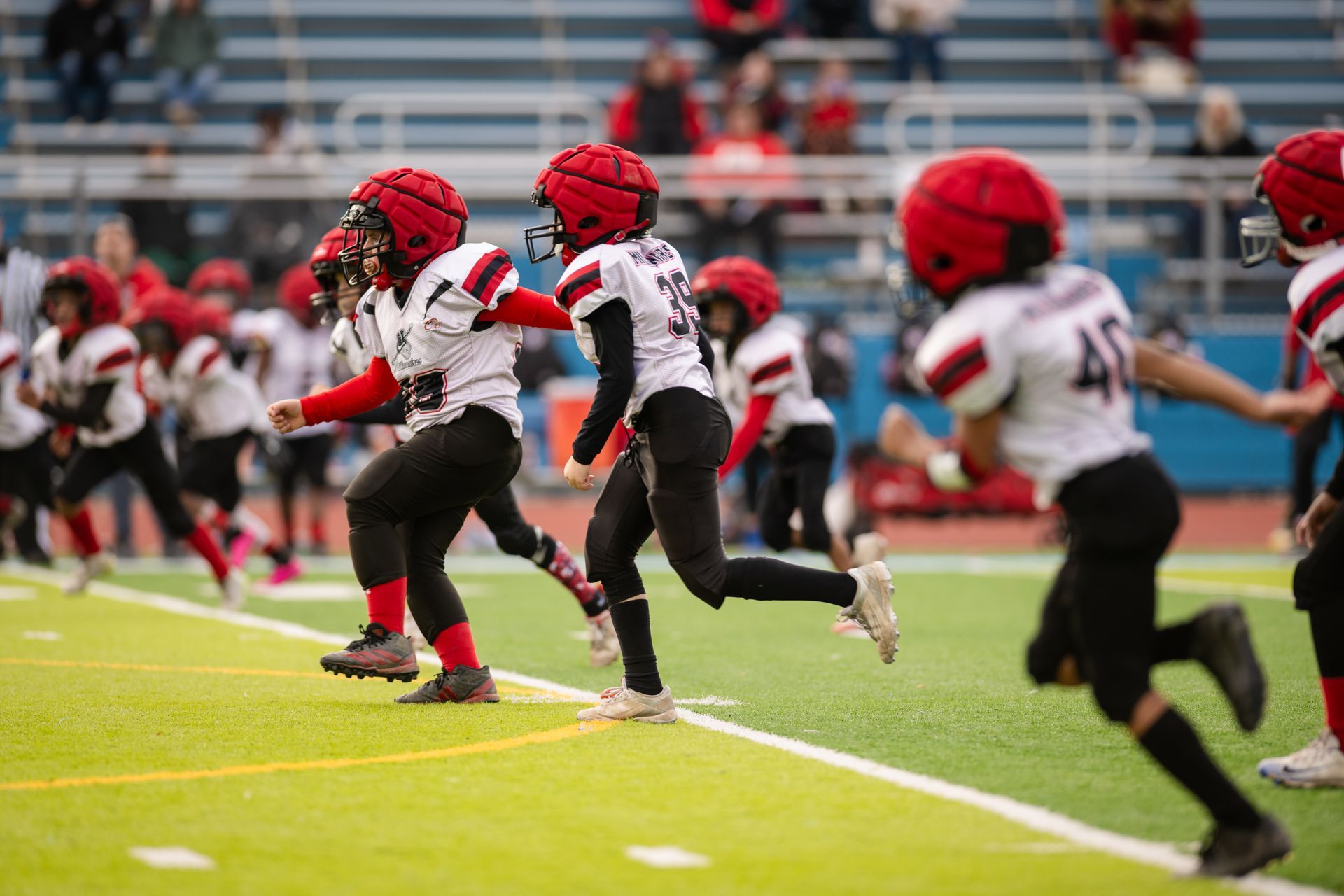 Football players in white jerseys and black pants running downfield after a kickoff.