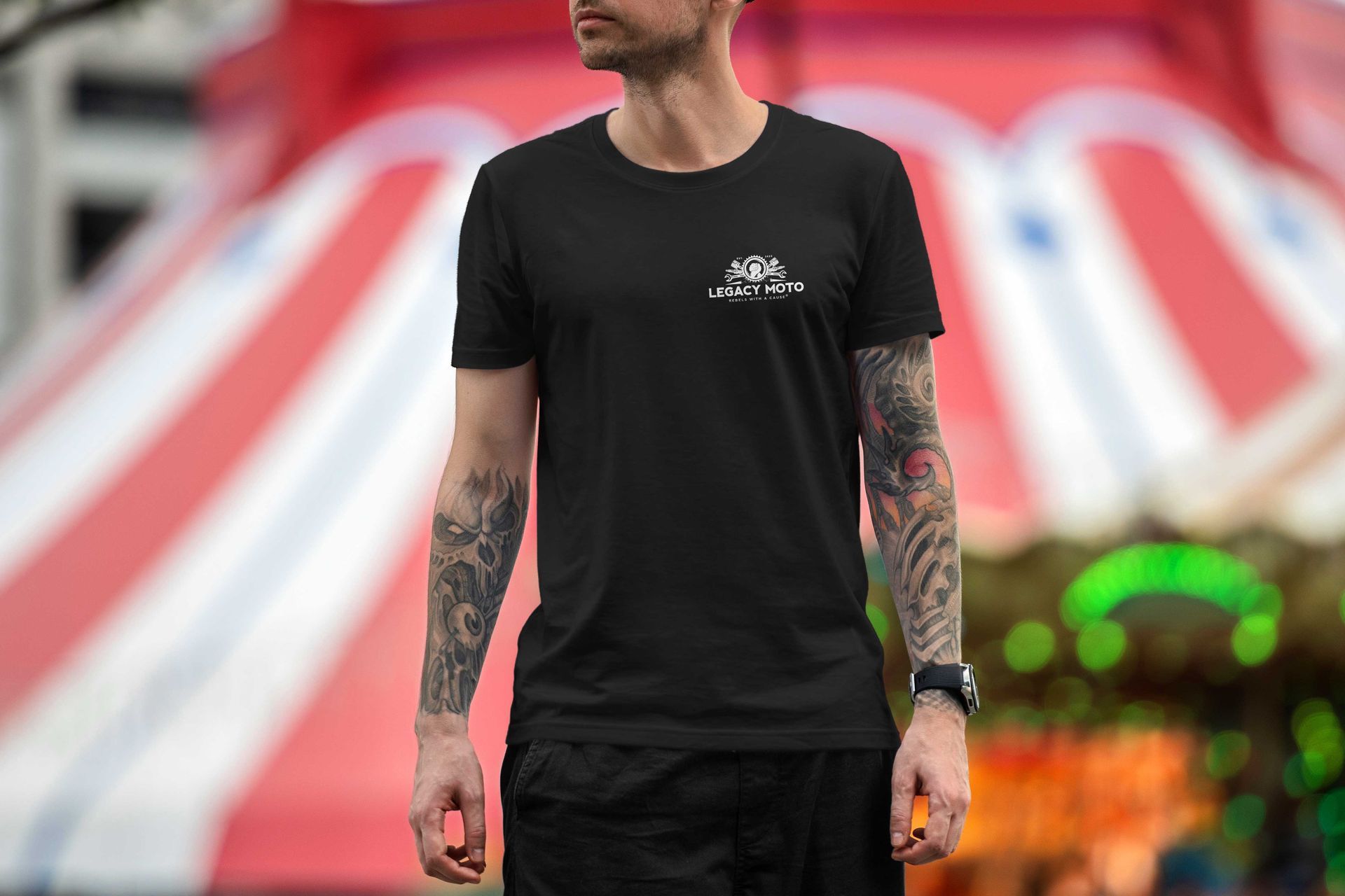 Tattooed man in a black T-shirt standing before a blurred red and white stage backdrop