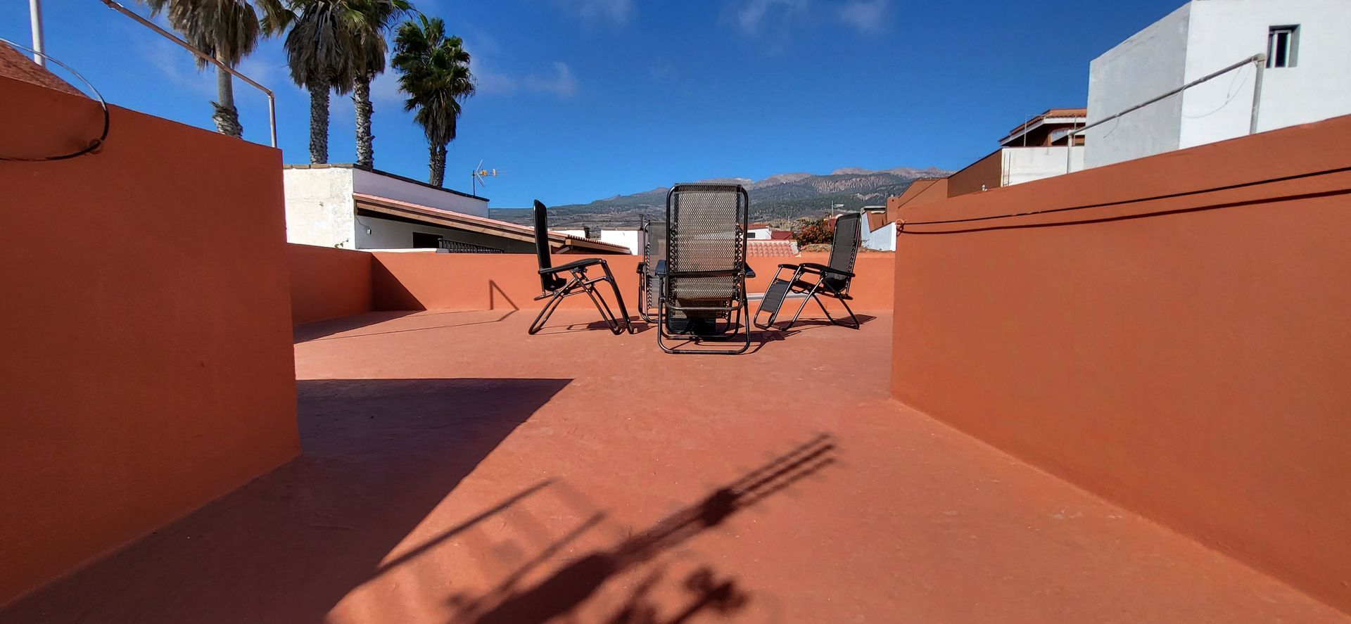 Eine Terrasse auf dem Dach mit Tisch und Liegestühlen an einem sonnigen Tag.