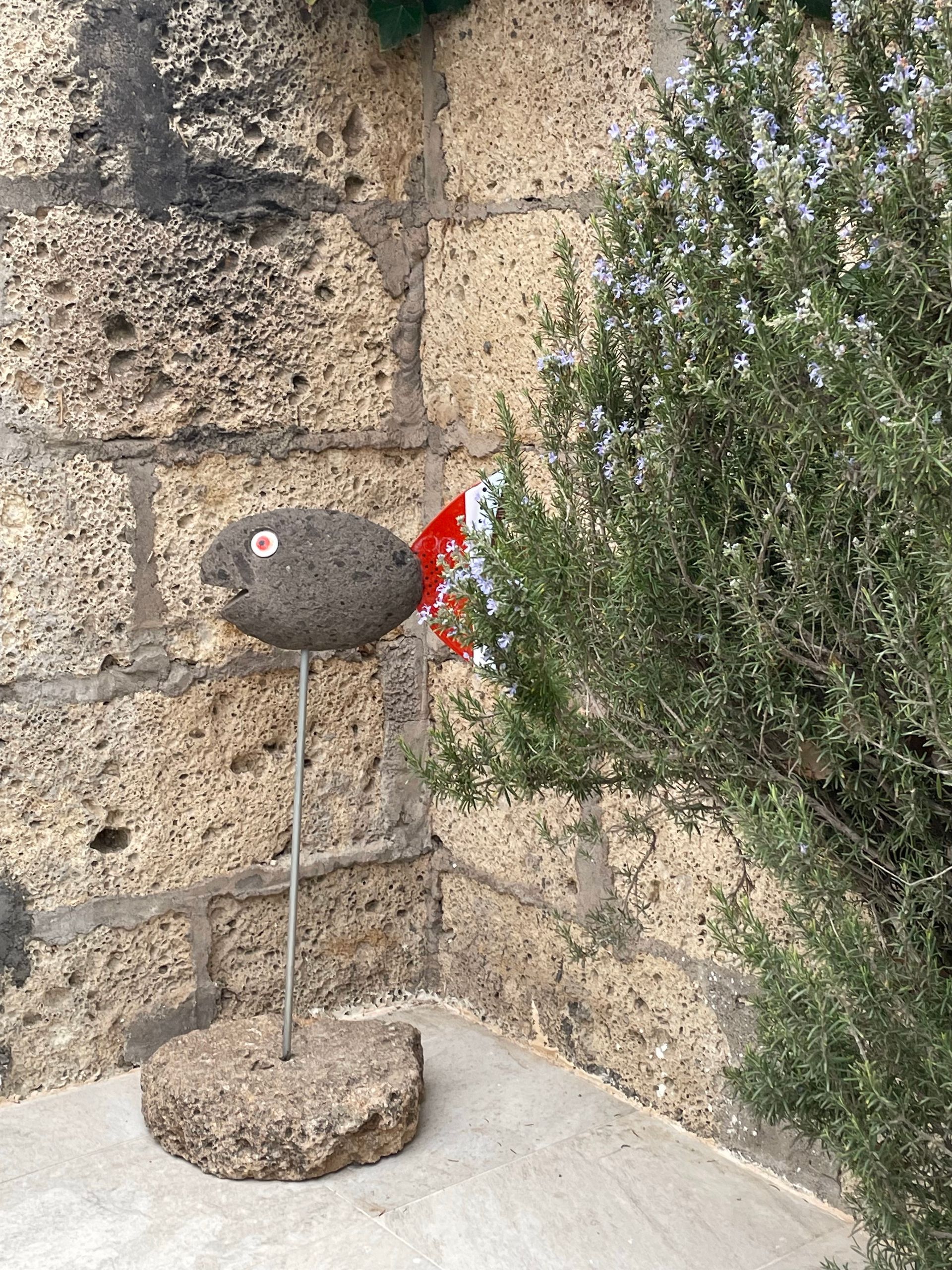 Vor einer Backsteinmauer steht die Statue eines steinernen Fisches auf einem Stock.
