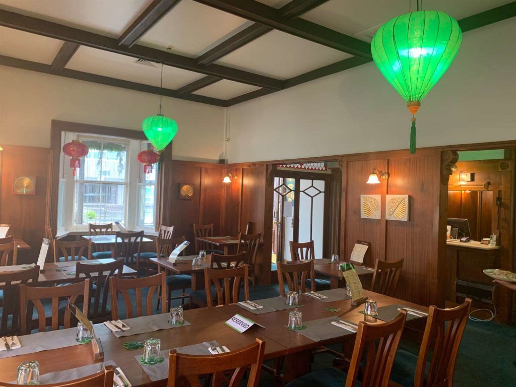 A restaurant with tables and chairs and green lanterns hanging from the ceiling.
