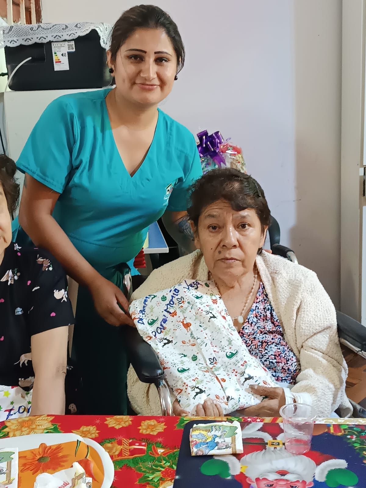 Dos mujeres sentadas en una mesa con comida, una de pie junto a la otra, sonriendo.