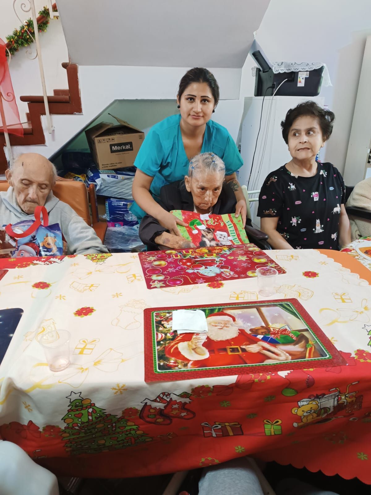 Cuatro personas se reunieron en el interior, alrededor de un mantel rojo festivo, posando junto a una mesa decorada.