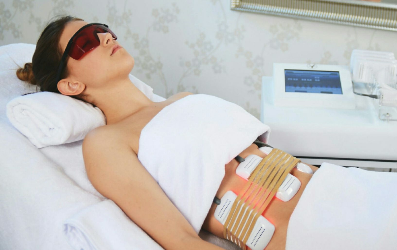 Spa treatment with a handheld device massaging a woman's abdomen while she lies under a white towel