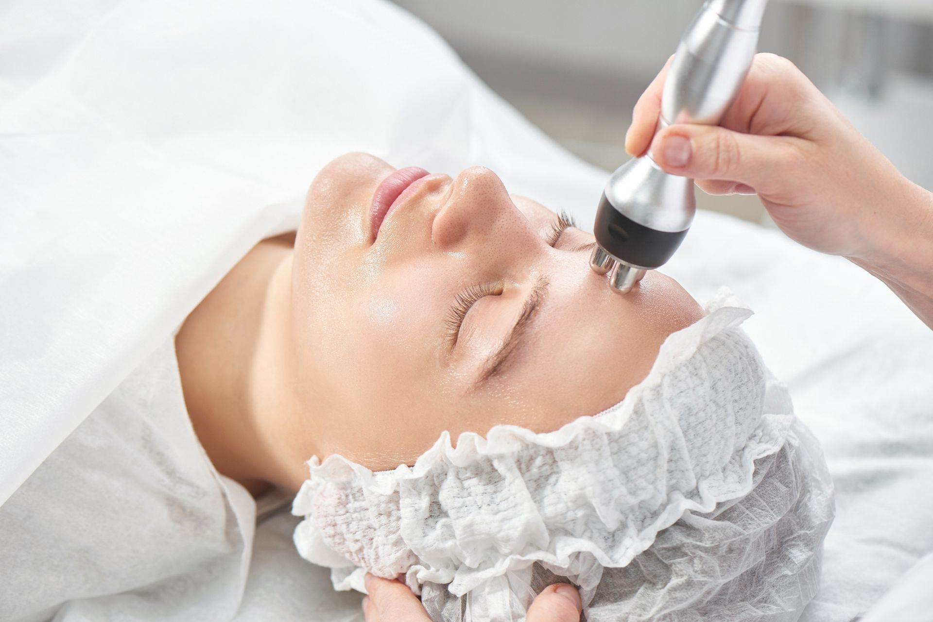 Facial treatment with a handheld skincare device on a client wearing a white headband