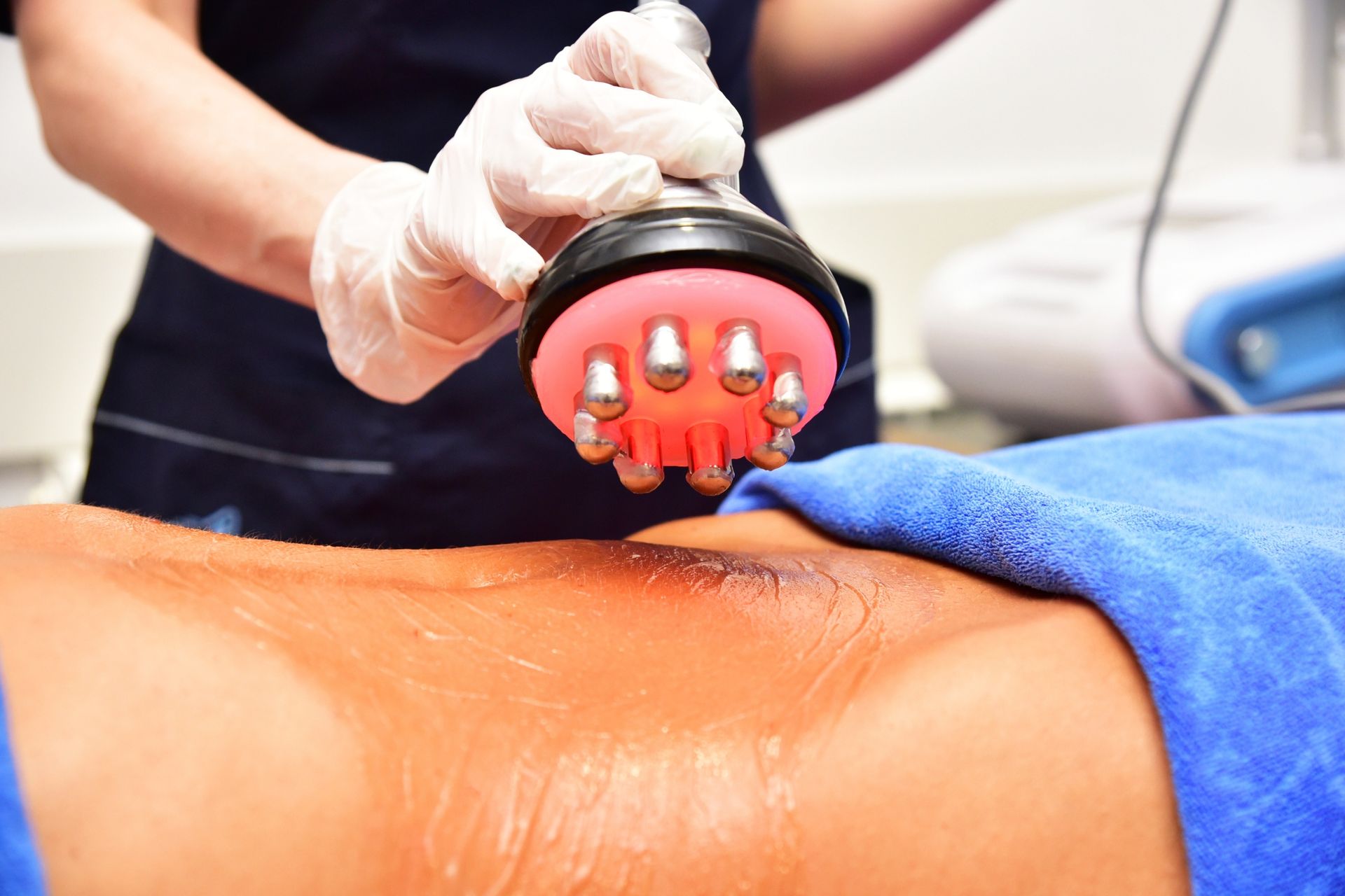 Massage therapist using a red handheld massager on a person’s oiled back