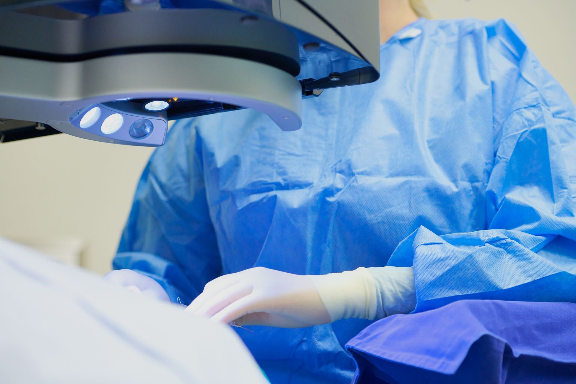 Surgeon in blue sterile gown and gloves under an operating room surgical light