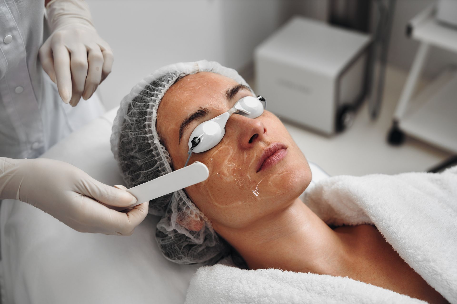 Facial treatment in a spa, with a woman wearing eye pads while a practitioner applies a facial mask to her cheek.