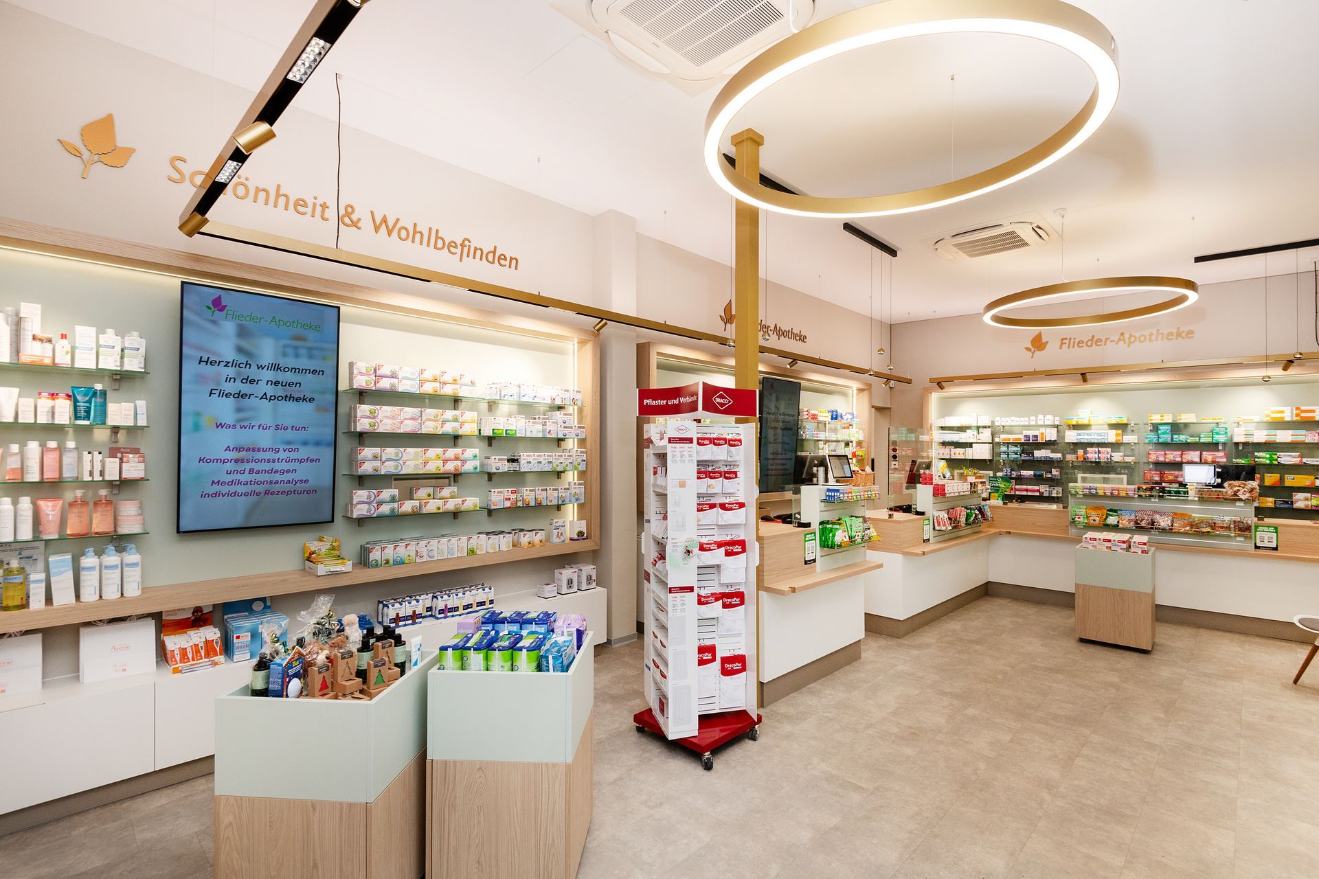 Interieur einer Apotheke mit Regalen voller Produkte und einem zentralen Präsentationsständer, neutrale Farbtöne, modernes Design.