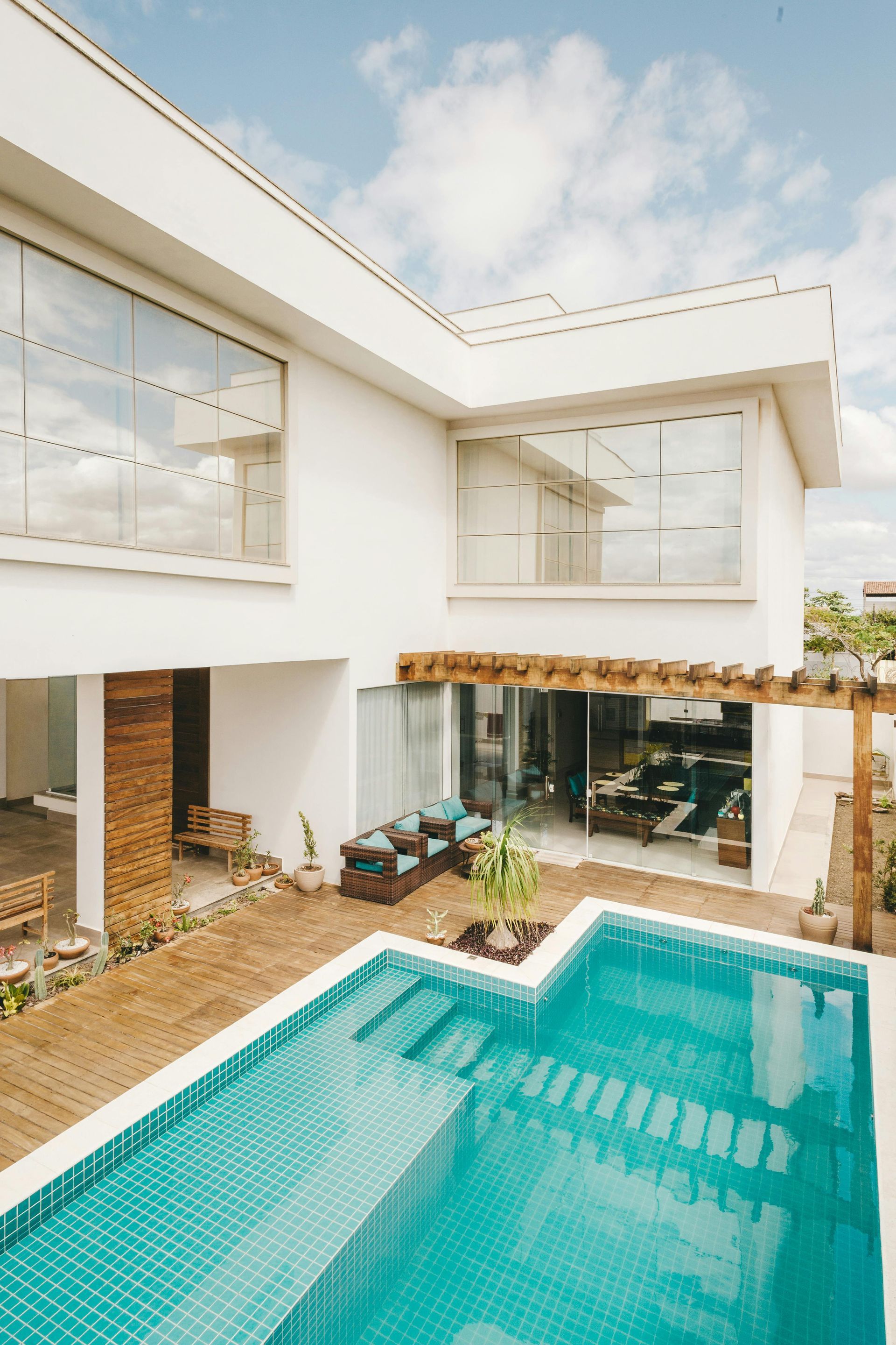 White modern house with a pool. Large windows, turquoise pool, wooden pergola, blue sky.
