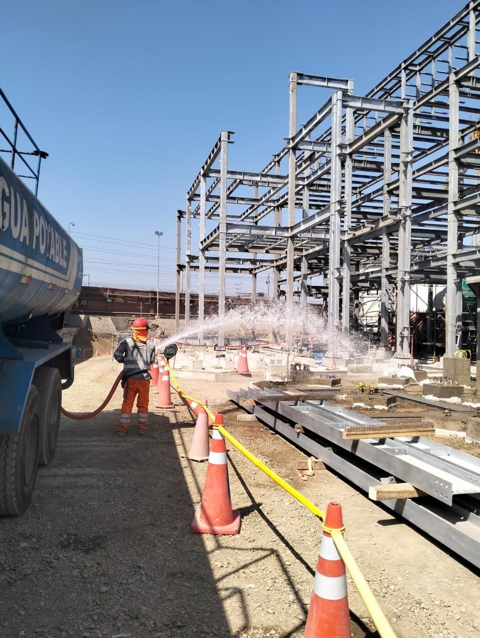 Un trabajador rocía agua sobre una estructura de acero en una obra de construcción junto a un camión grande.