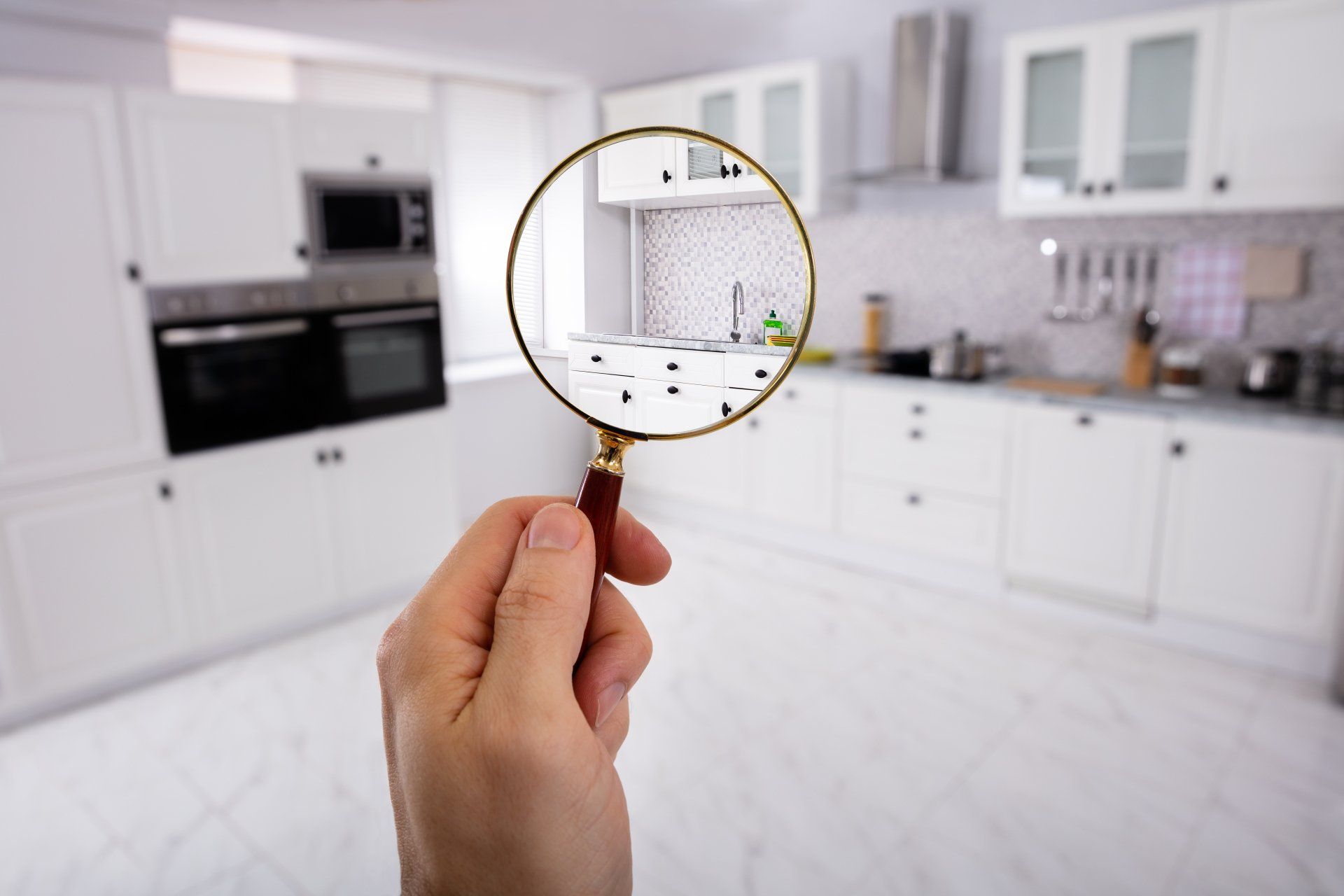 Main tenant une loupe sur un intérieur de cuisine blanc.