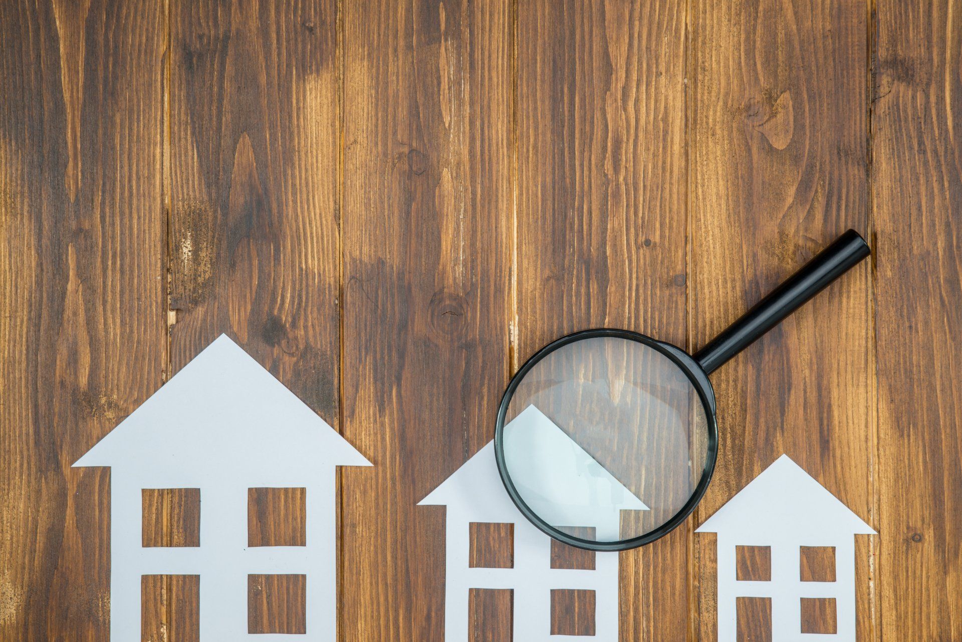 Trois maisons en papier et une loupe sur une table en bois.