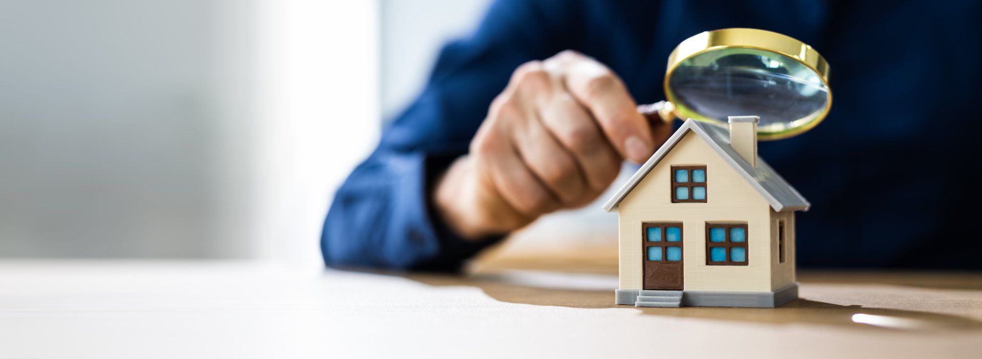 Une personne tenant une loupe au-dessus d'une maison miniature, probablement pour l'inspecter ou l'évaluer.