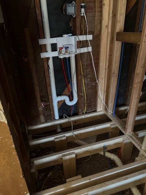Red and blue PEX plumbing pipes attached to vertical wooden wall studs inside a construction site.