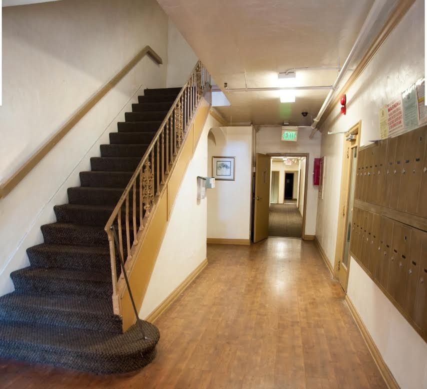 Interior hallway with staircase, mailboxes, and doors; wooden floors and railings.