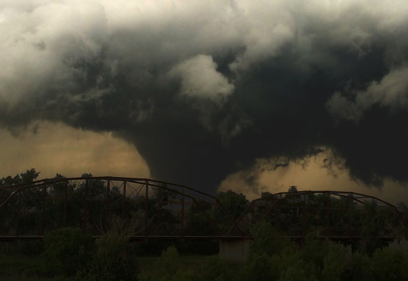 A large tornado is moving over a bridge in the distance.
