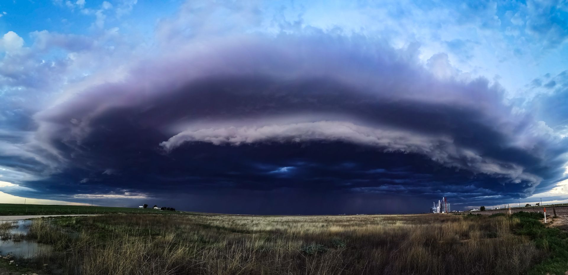 A large storm cloud is moving over a field.