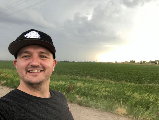 A man wearing a hat is standing in front of a field.