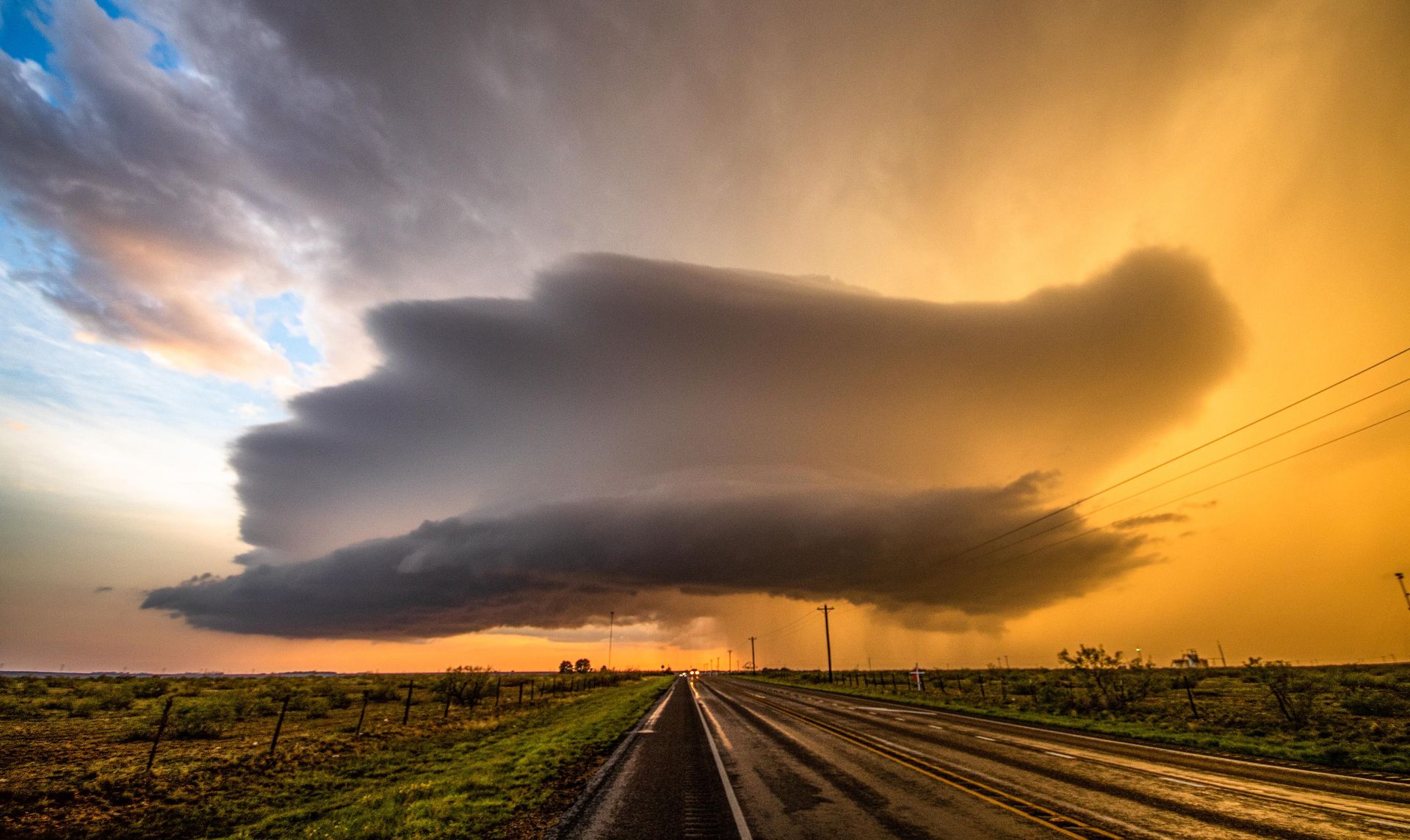 A storm cloud is moving over a train track at sunset.